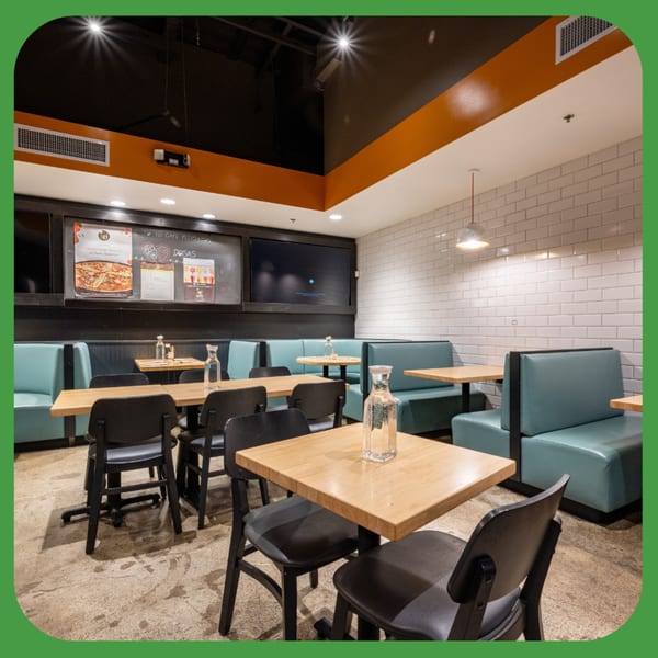 Interior of ID Cafe with light wood tables, black chairs, and teal booth seating against white subway tile.