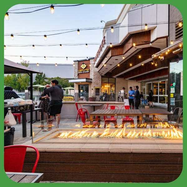Outdoor patio with string lights, a long fire pit, and people dining at tables.
