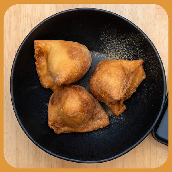 Three golden-brown fried dough pastries, possibly Indian puri or bhature, in a black bowl on a wooden table.
