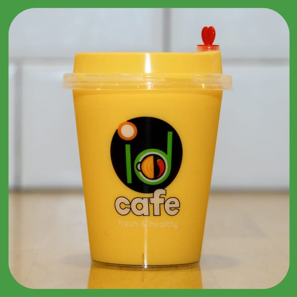 A yellow ID Cafe cup with a red heart-shaped stopper, filled with a yellow beverage.
