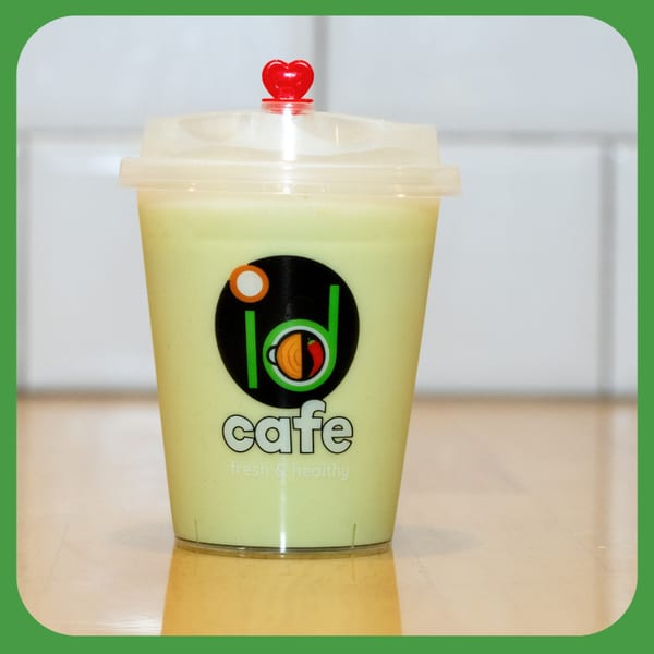 A light green drink in a clear plastic cup with a red heart on the lid, featuring the ID Cafe logo.