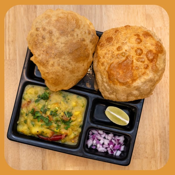 Two golden-brown Indian puri breads with a side of potato curry, lime, and chopped red onions.
