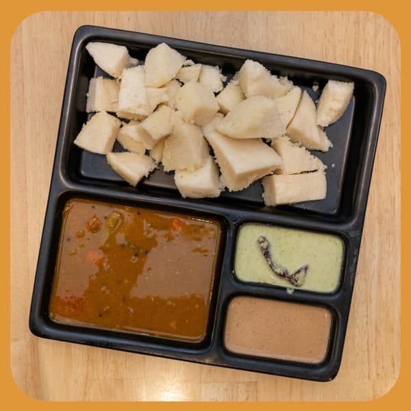 ID Cafe's Indian dish with chopped idli, sambar, and two chutneys in a black tray.