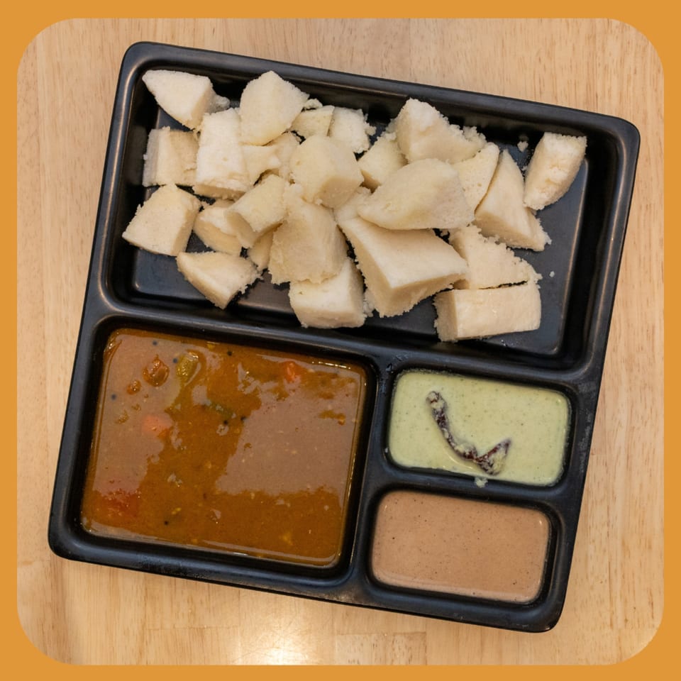 ID Cafe's Indian idli, cut into pieces, served with three different chutneys in a black tray.