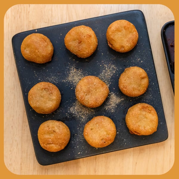 Nine golden-brown Indian cafe fritters, dusted with spices, arranged on a black rectangular plate.